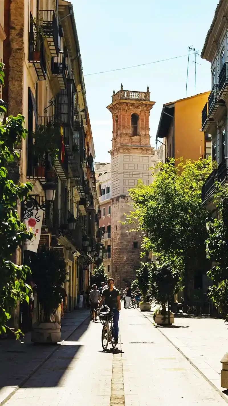 Hombre montando bicicleta en calle estrecha de Valencia rodeada de edificios