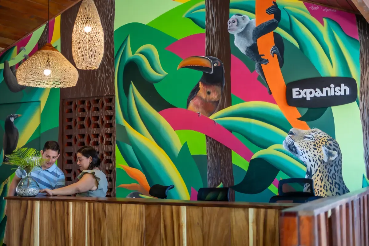 costa-rica-samara-reception-jungle-mural.webp Expanish Costa Rica reception desk in Samara with colorful jungle mural featuring toucan, monkey, and jaguar