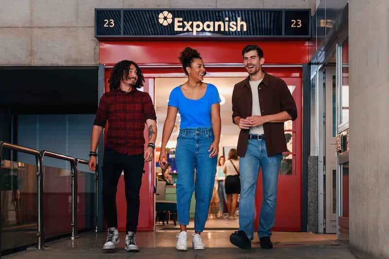 Three smiling adult students walking out the door of the Expanish Madrid school.