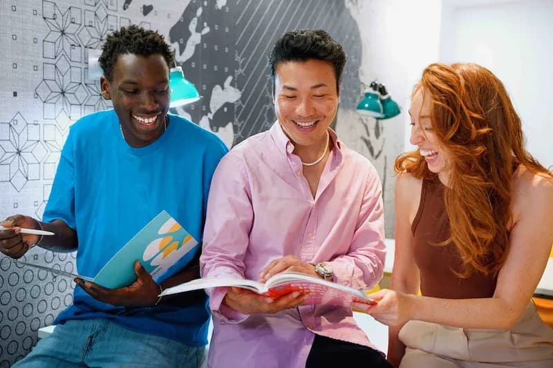 Three adult students laughing together while reading books at the Expanish Madrid school.