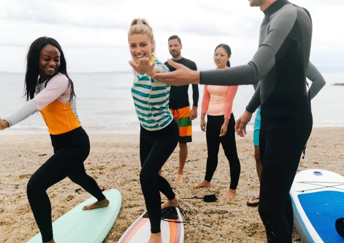 Students practicing surf stances on the beach with an instructor guiding them.