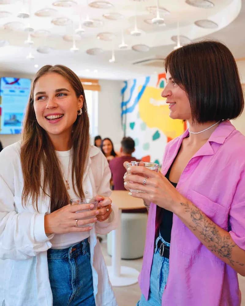 Two adult students at Expanish Málaga smiling and chatting while enjoying drinks in the school common area.