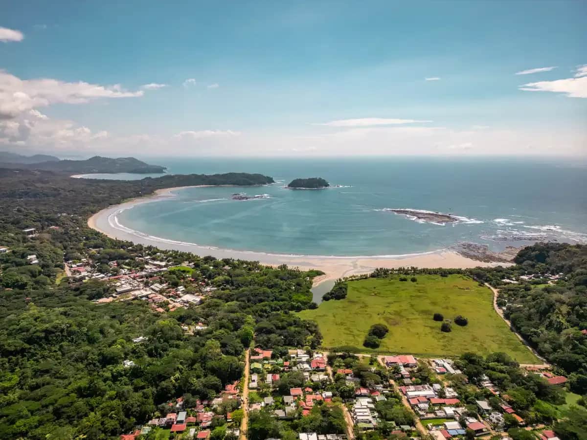 Aerial view of the coastline and town of Sámara, Costa Rica, surrounded by lush greenery and the Pacific Ocean.