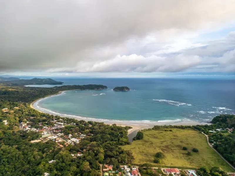 Aerial view of a quiet bay in Costa Rica with a curved beach, ocean waves, and lush greenery.
