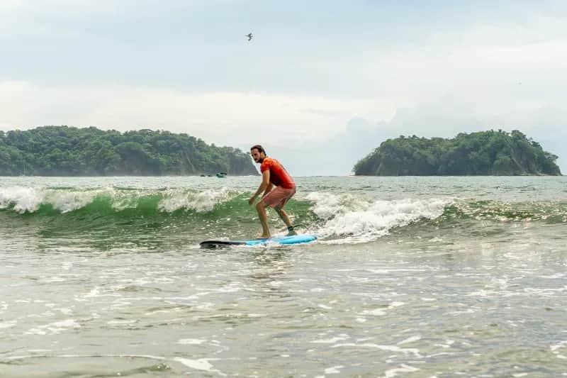 Student surfing a small wave at Samara Beach with green hills in the background.
