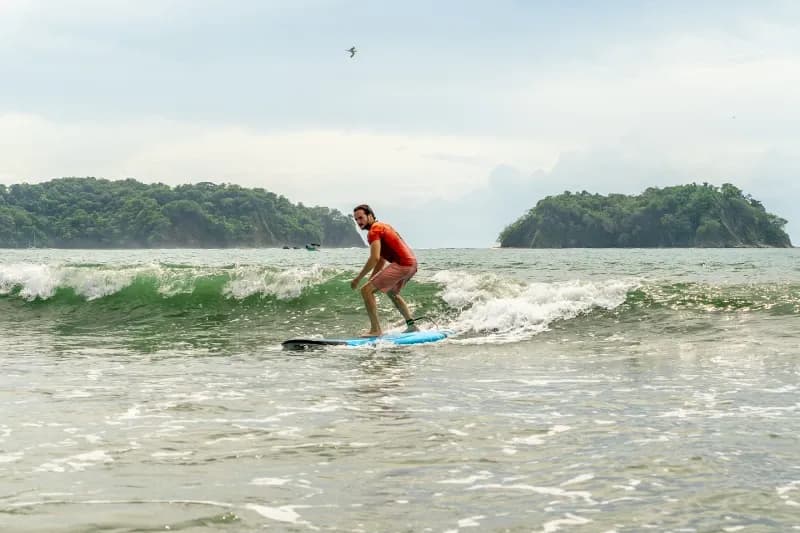 Student surfing a small wave at Samara Beach with green hills in the background.