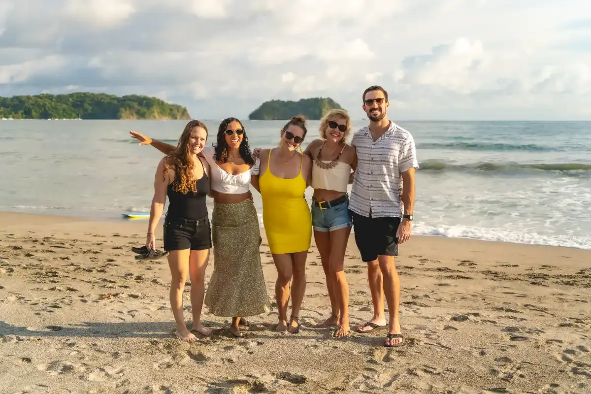 Group of Expanish students smiling together on a sandy beach in Costa Rica with the ocean and green islands in the background.
