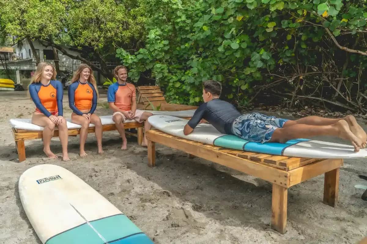 Expanish students learning surfing fundamentals on the beach in Sámara, Costa Rica, listening to an instructor during a beginner surf lesson.
