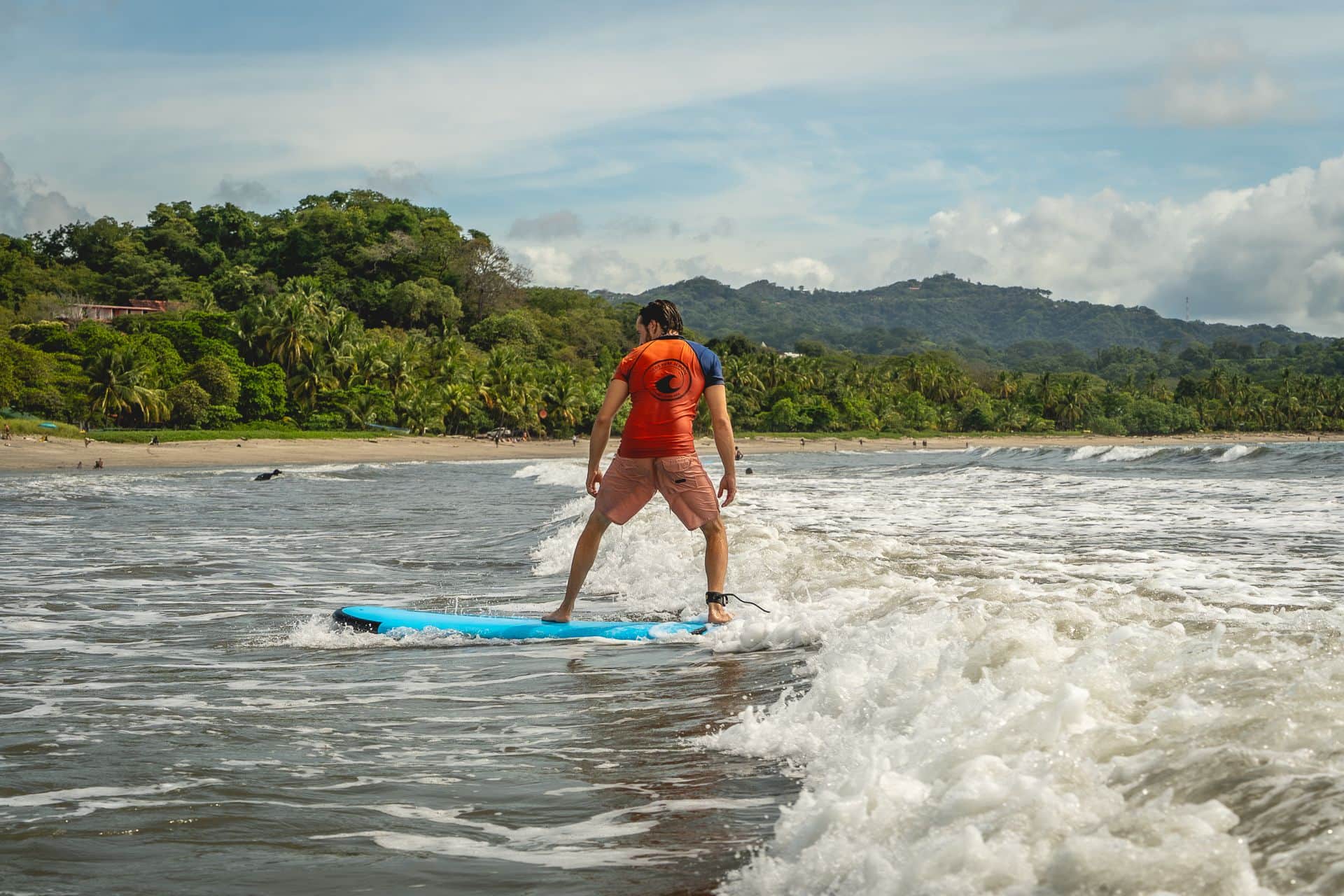Student standing on a surfboard riding a small wave at Samara Beach in Costa Rica.