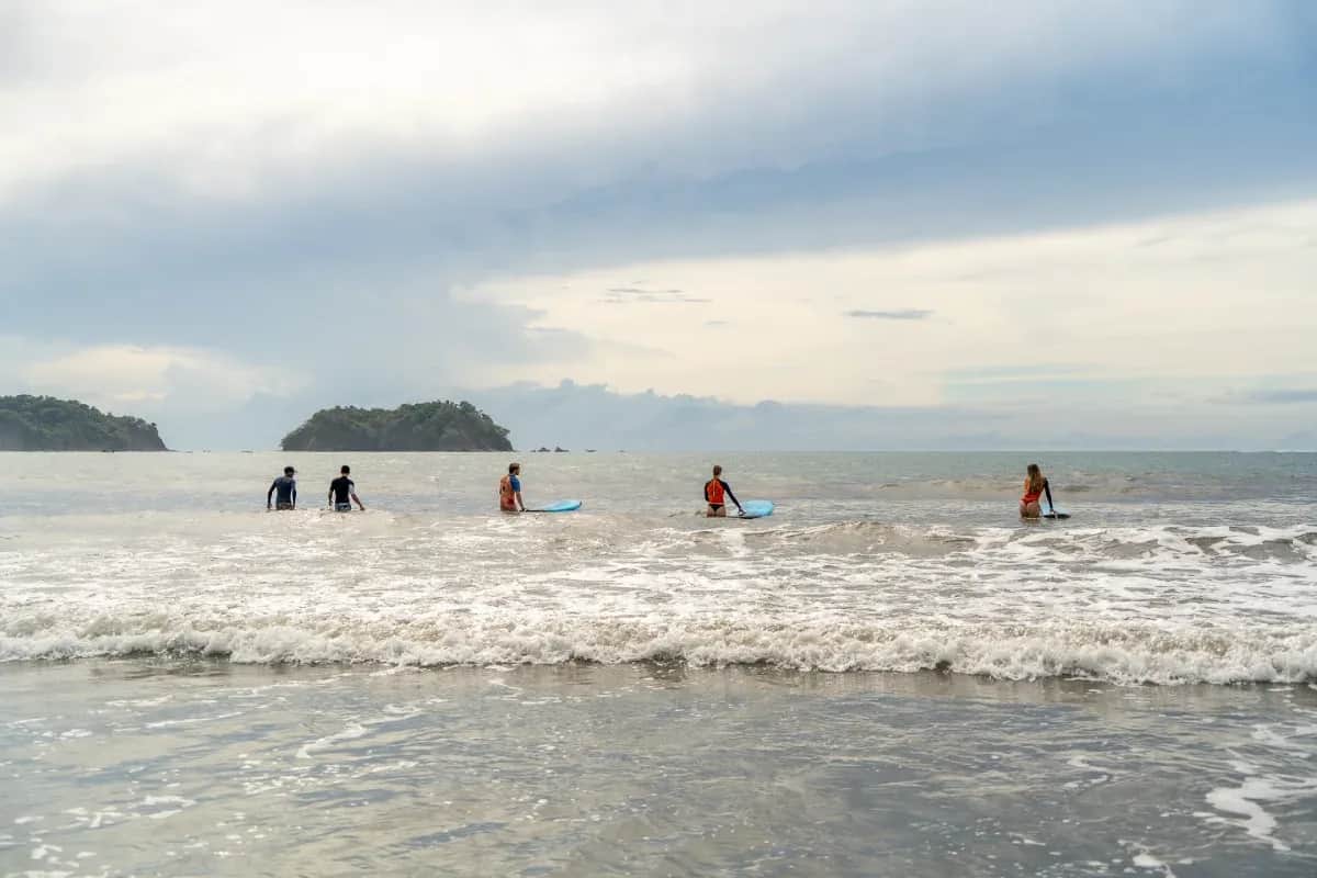 Expanish students carrying surfboards as they walk into the ocean to surf the waves in Sámara, Costa Rica.