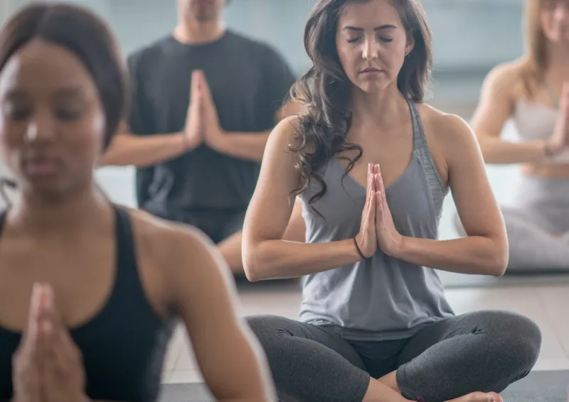 Students sitting cross-legged with hands in prayer position during a calm yoga class.