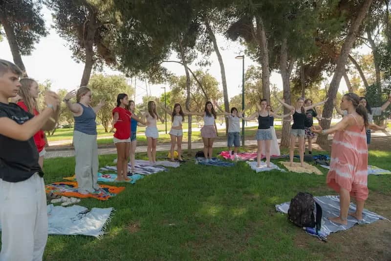 Expanish summer camp students participating in a guided outdoor mindfulness activity in a park.