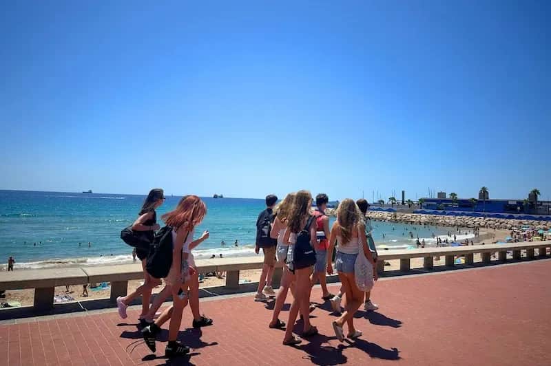 Expanish Barcelona summer camp students walking along the beachfront on a sunny day.