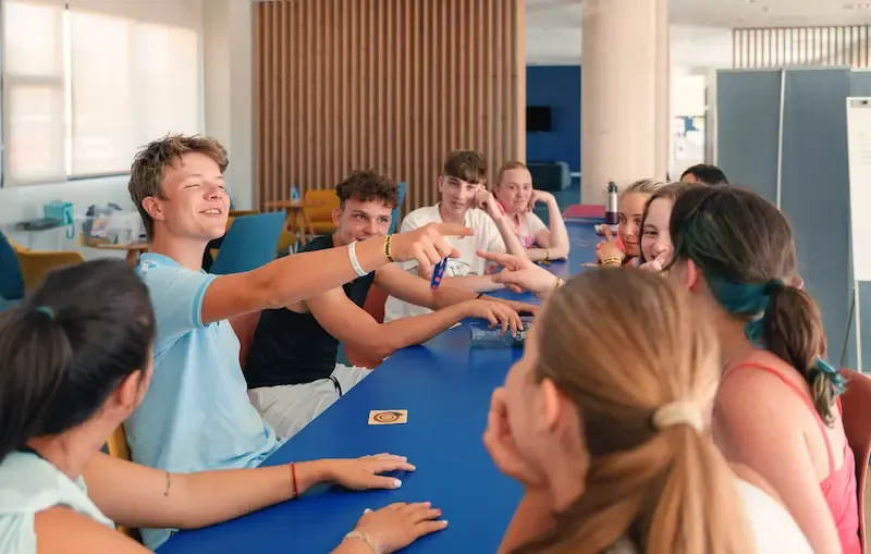 Expanish summer camp students engaged in a lively group discussion around a classroom table.