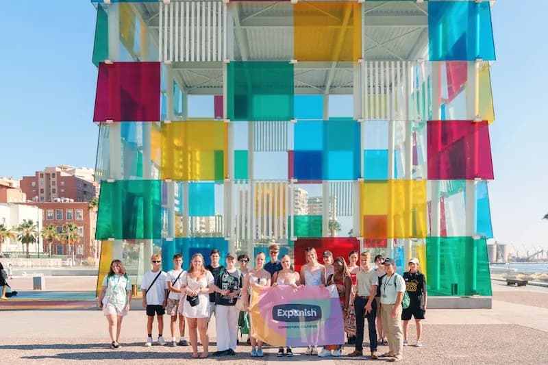 Expanish summer camp students posing with a flag in front of the colorful Centre Pompidou Málaga.