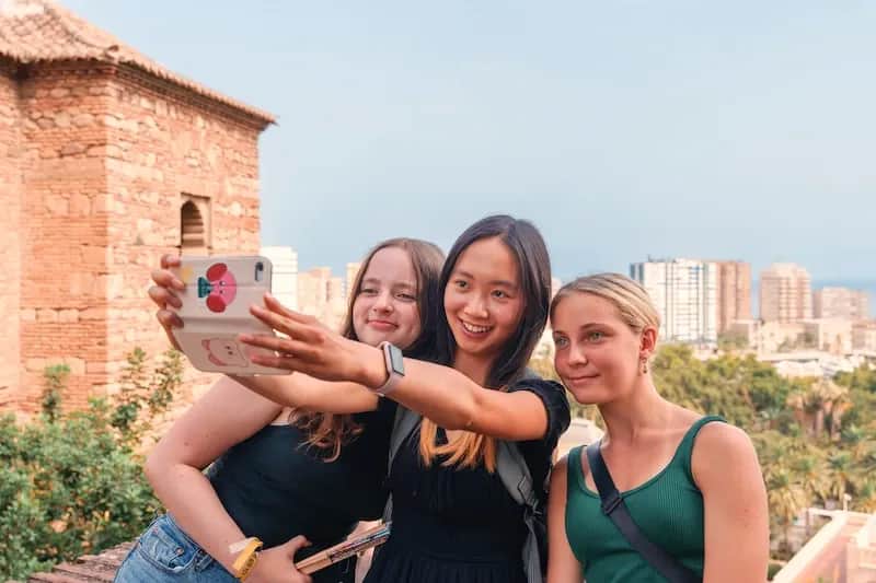 Three Expanish summer camp students taking a selfie at a historic site in Málaga.