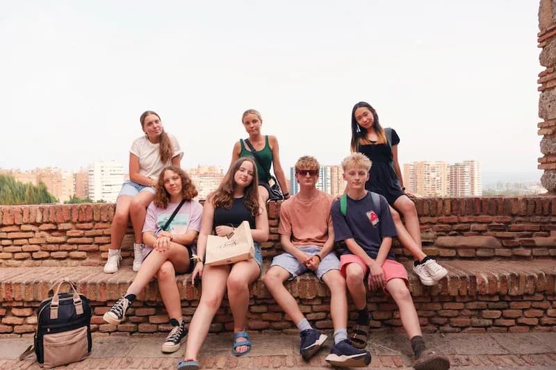 Expanish summer camp students sitting together at a historic viewpoint in Málaga.