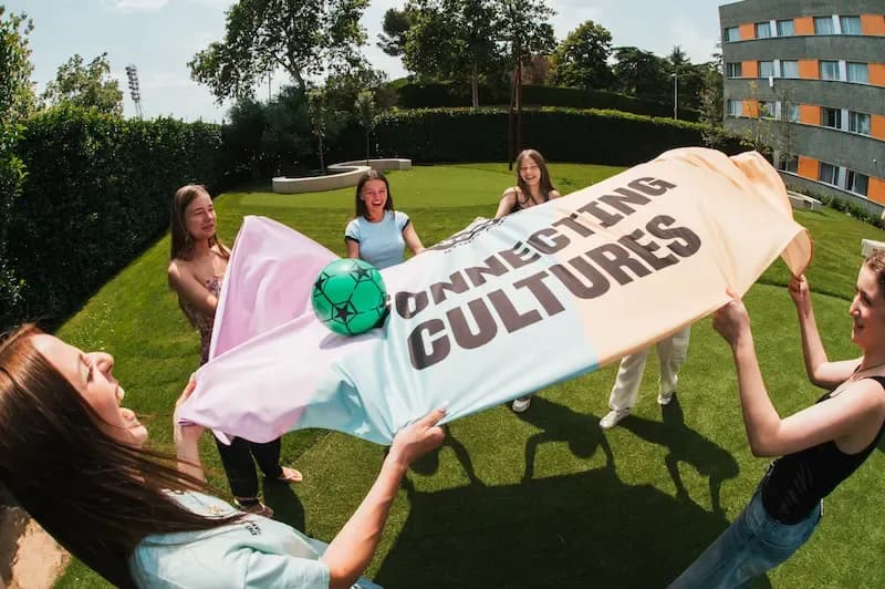 Students at an Expanish summer camp playing an outdoor game with a colorful Connecting Cultures banner.